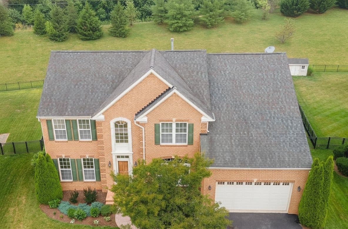 A brick colonial home with a weathered, discolored roof before renewal